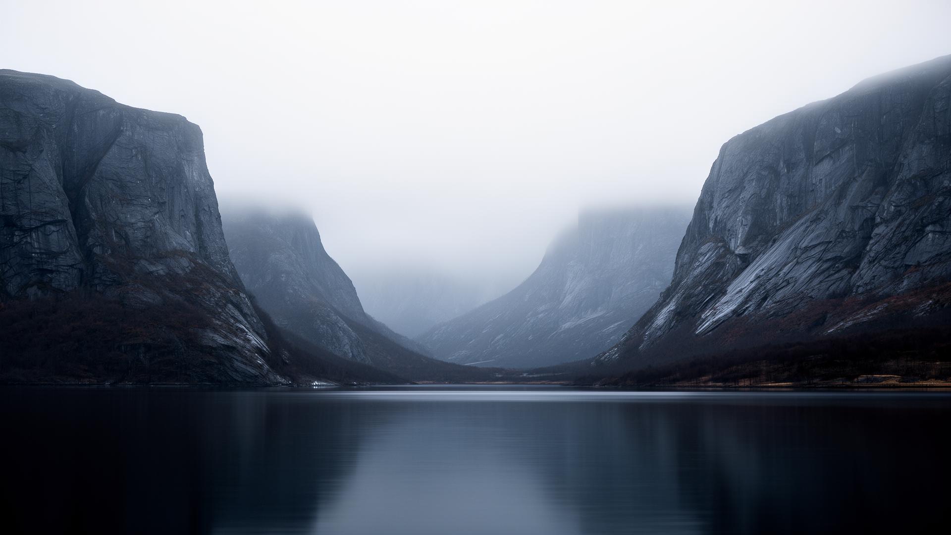 A still grey fjord at dawn — mist between cold stone cliffs, the moment cold air meets the sea.